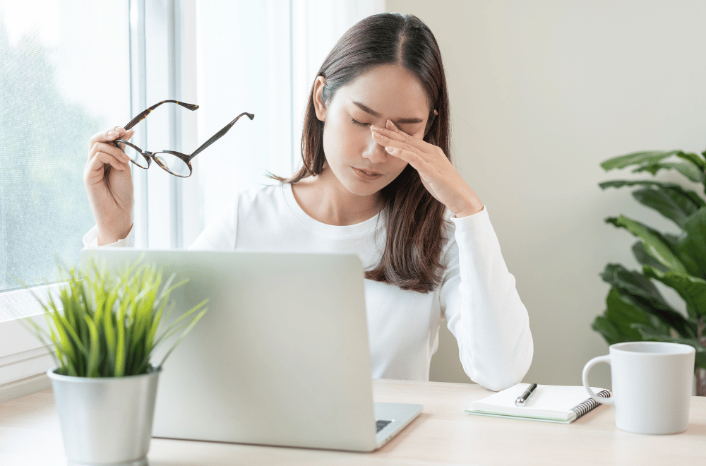 a young woman taking off her glasses and looking uncomfortable while using a computer