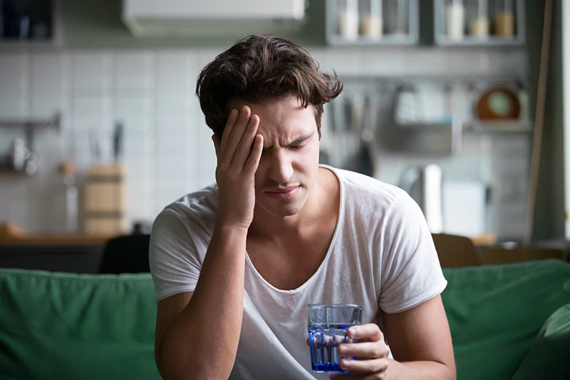 a man suffering from a migraine and sitting at home with a glass of water