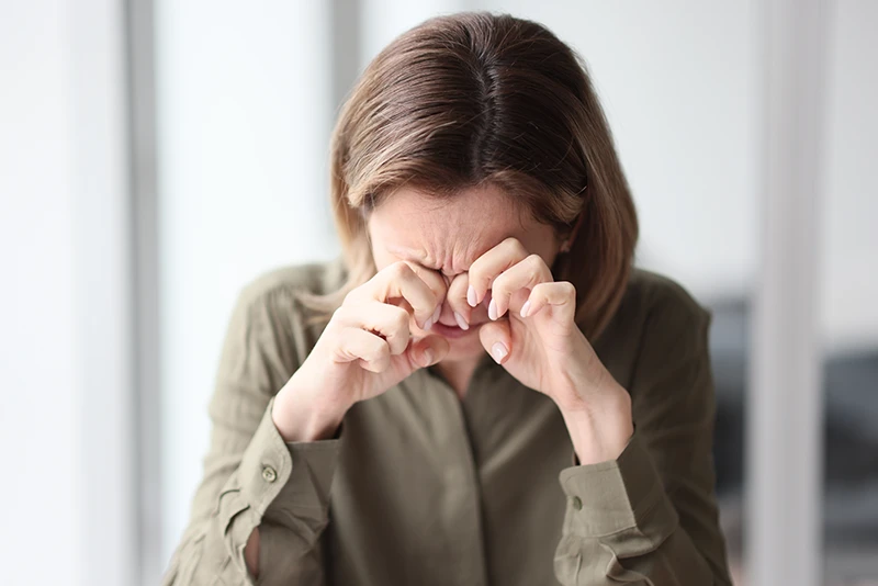 a woman holding her hands to her eyes and looking uncomfortable